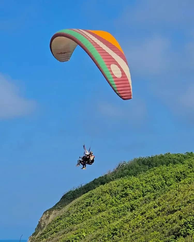 Paraglider gliding above a green hill
