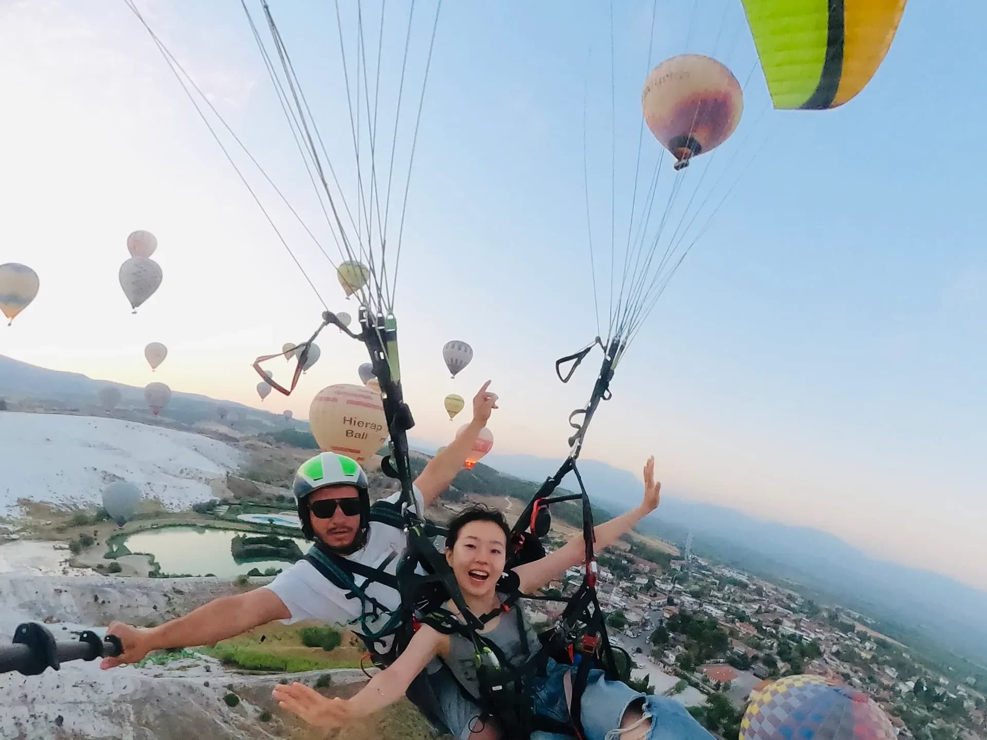 Tandem paragliding over Pamukkale with hot air balloons behind