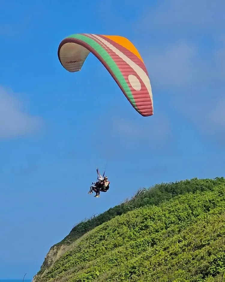 Paraglider gliding above a green hill